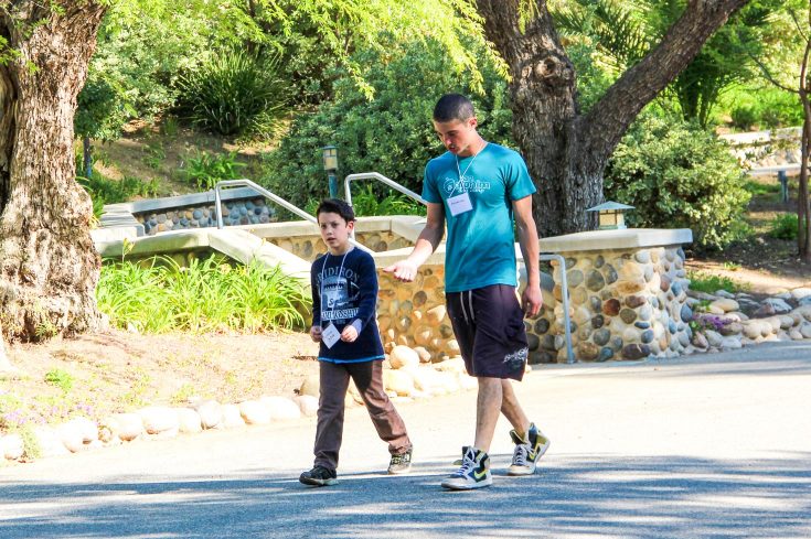 Young camper and older camper walking together on the campus