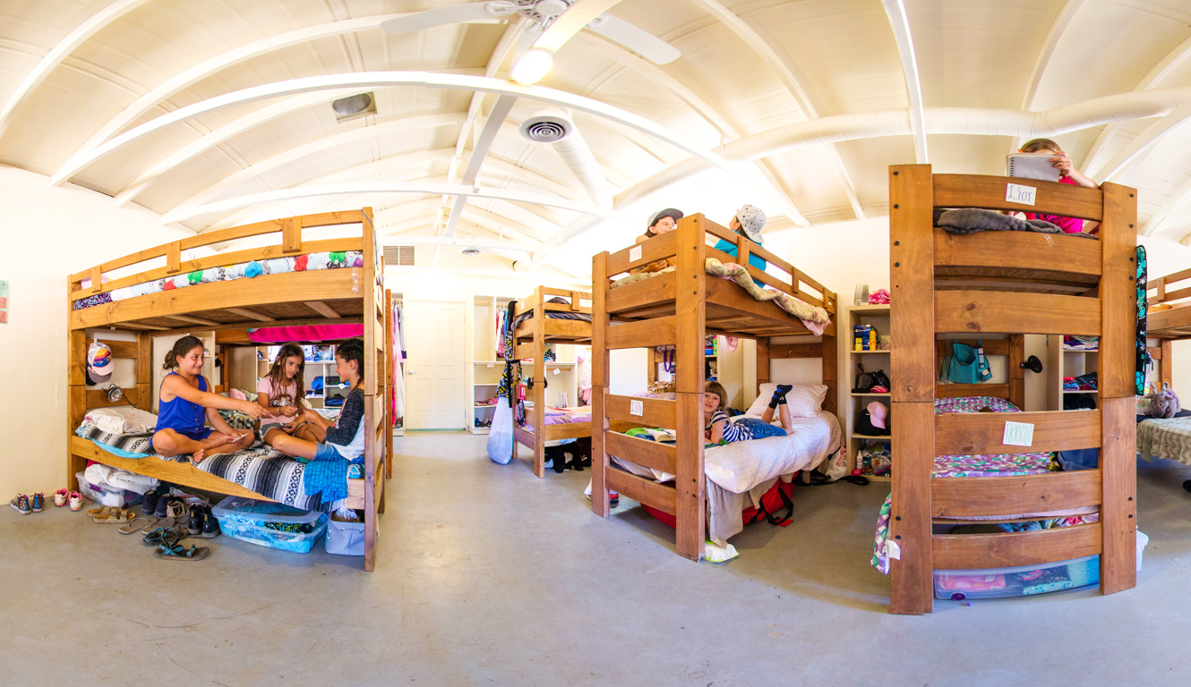 Panoramic photo of the inside of a bunk cabin with campers sitting in their bunks